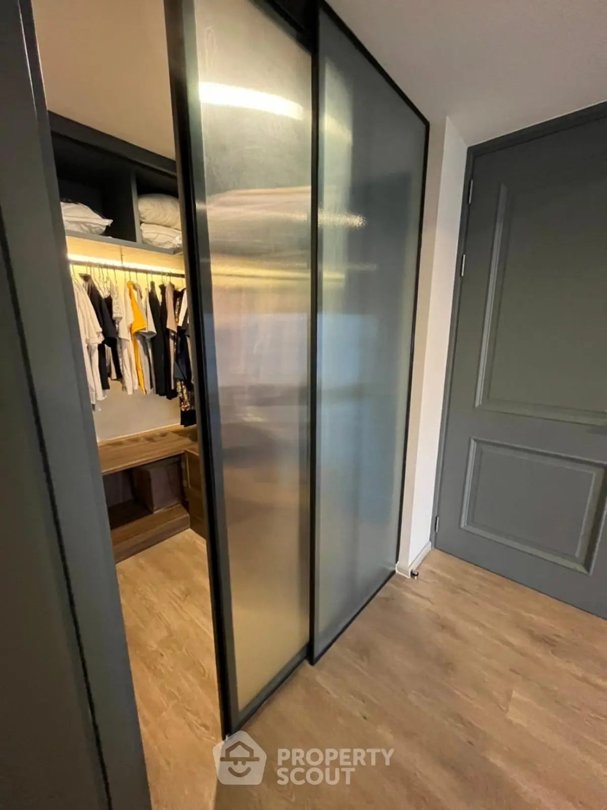 Modern walk-in closet with sliding frosted glass doors and wooden flooring