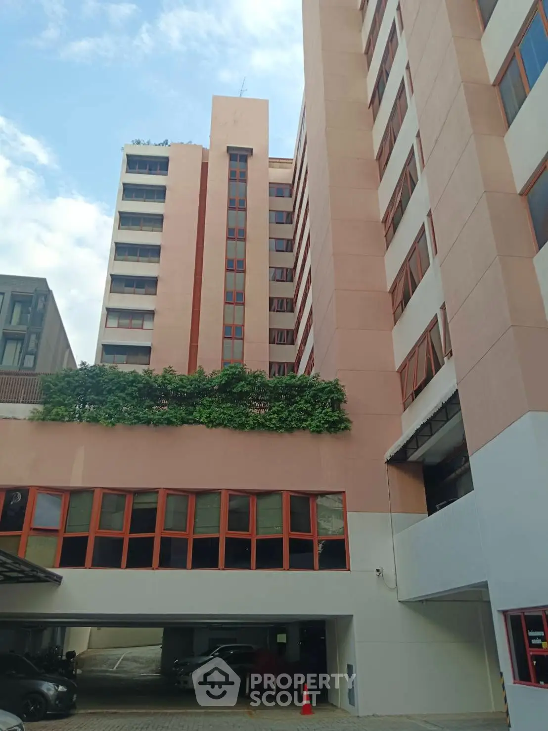 Modern multi-story building with parking area and lush greenery on facade.