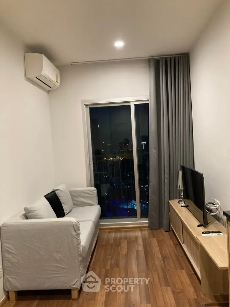 Cozy living room with modern decor, featuring a comfortable sofa, flat-screen TV, and city view from the balcony.