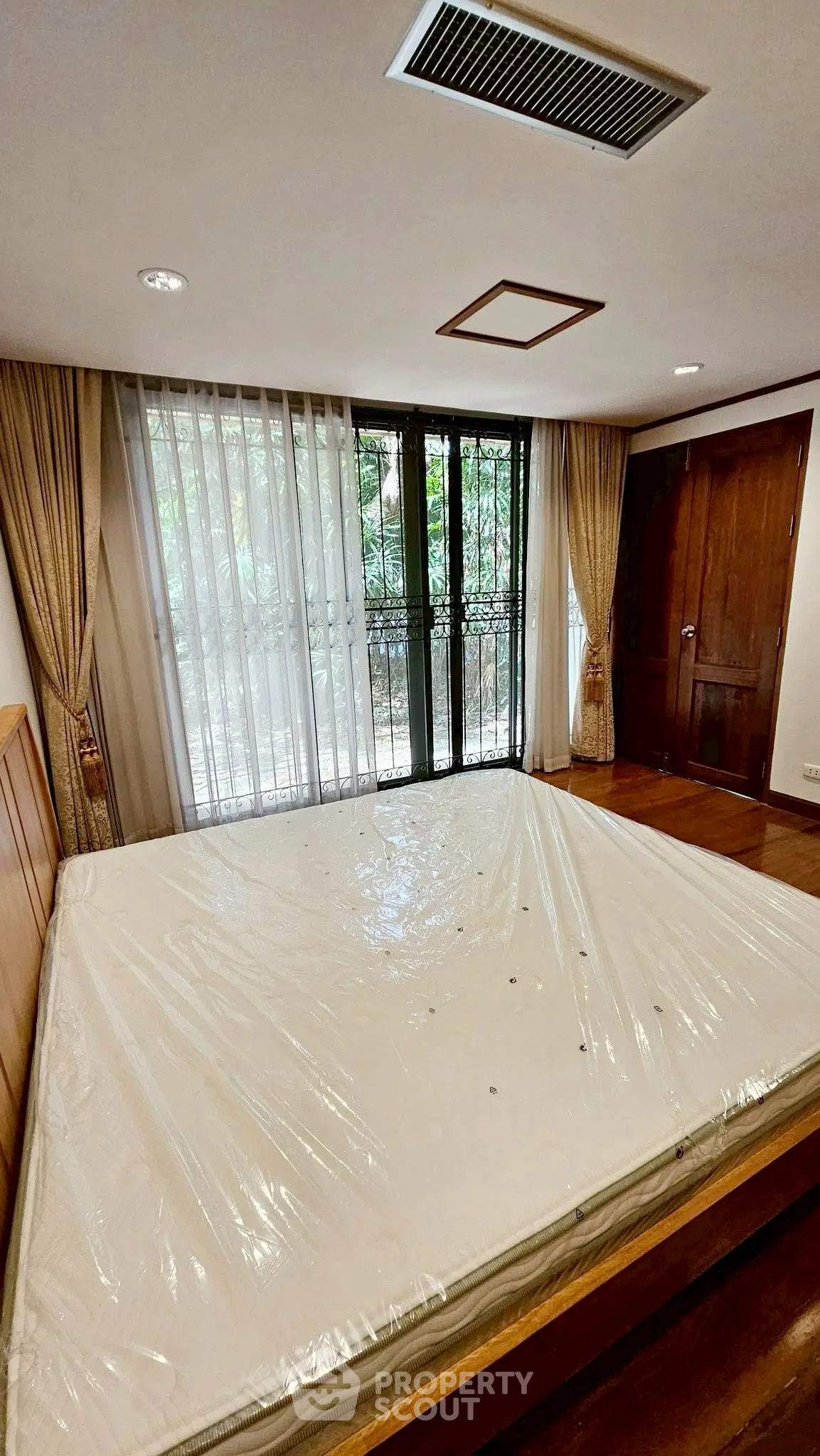 Spacious bedroom with large windows and elegant curtains, featuring a new mattress.