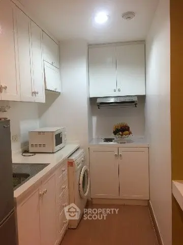 Compact kitchen with white cabinets, washing machine, and microwave in cozy apartment.