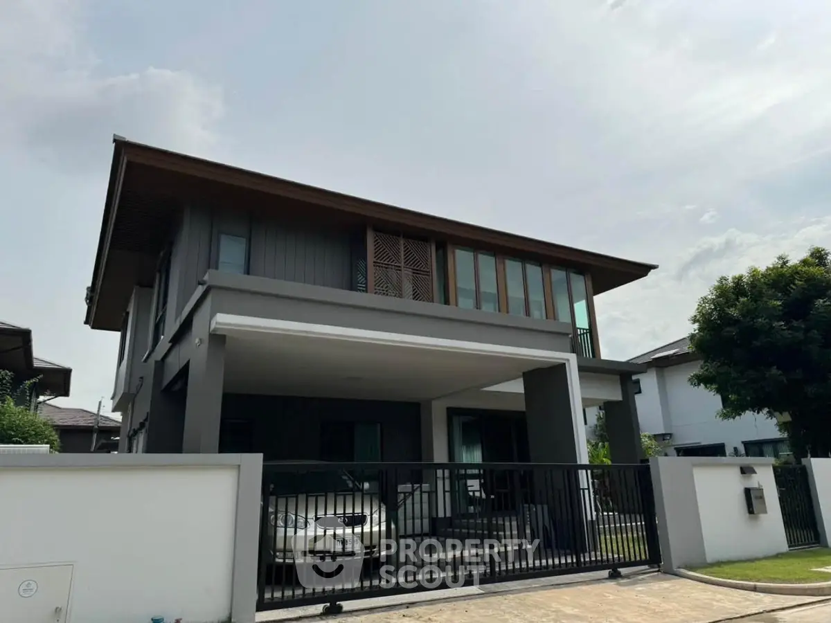 Modern two-story house with sleek design and gated driveway in suburban neighborhood.