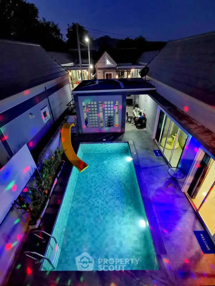 Stunning night view of a modern property with illuminated pool and colorful lights, perfect for entertaining.