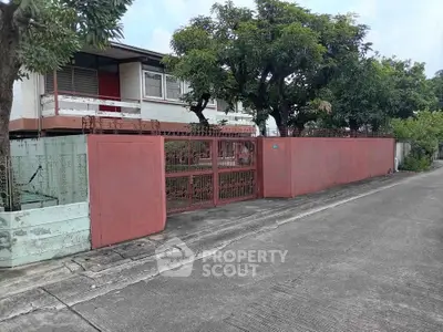 Charming suburban house with red gate and lush trees in a quiet neighborhood.