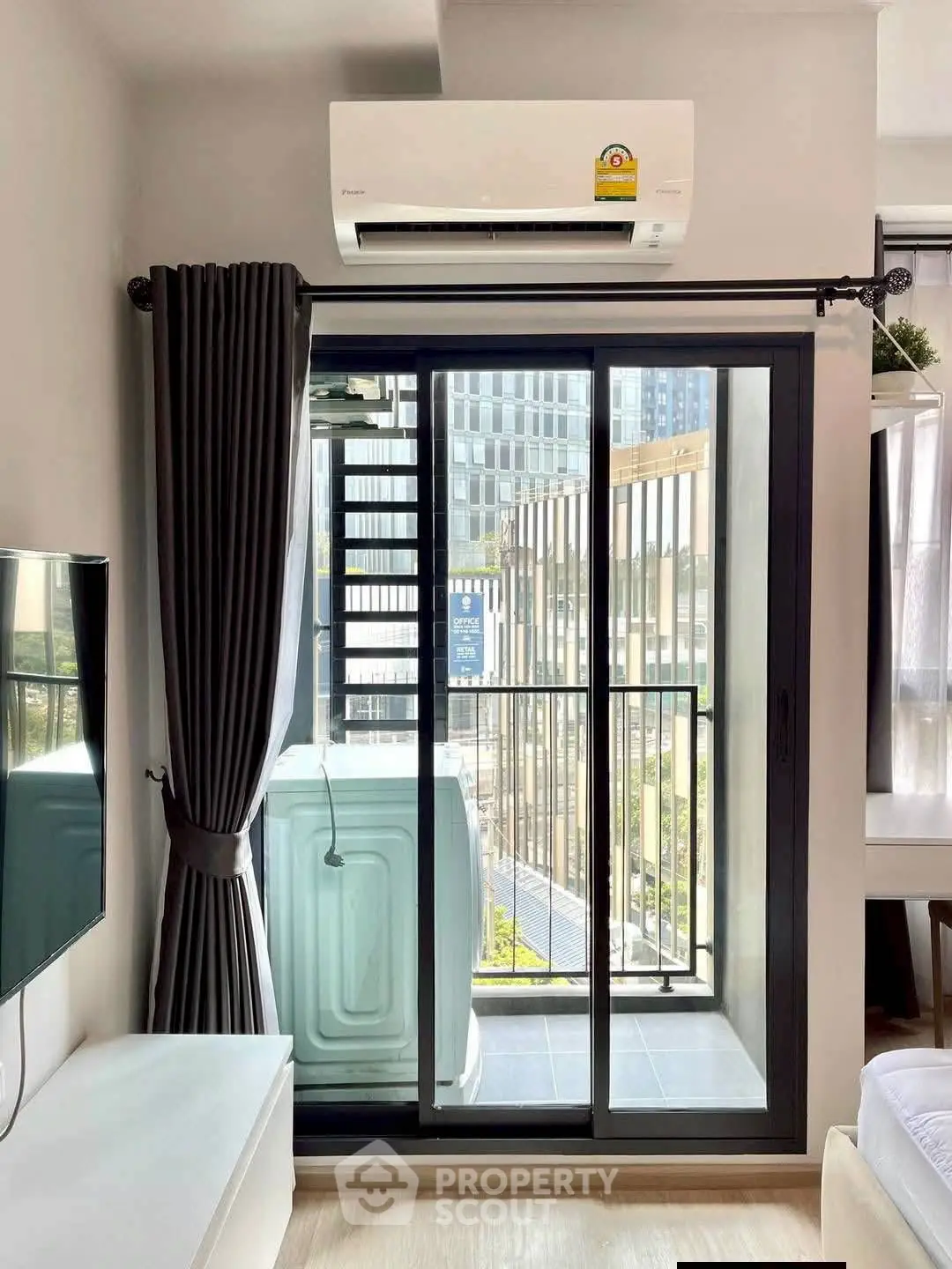 Modern apartment living room with balcony and washing machine, featuring sleek air conditioning unit.
