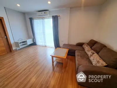 Spacious living room with polished wooden flooring, large comfortable sofa, and ample natural light from the sliding glass door leading to a balcony.