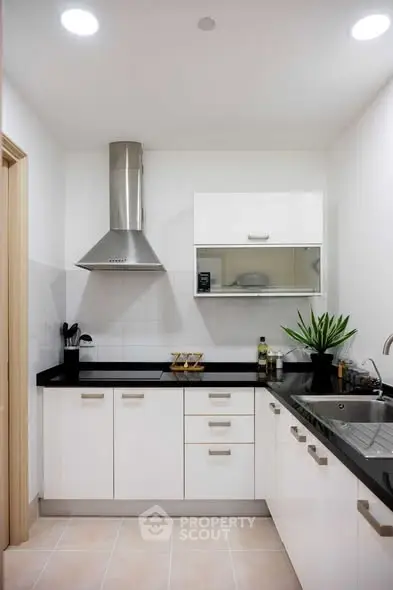 Modern kitchen with sleek white cabinets and black countertops, featuring a stainless steel range hood and sink.