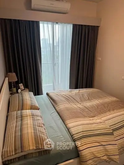 Cozy bedroom with striped bedding and natural light from window, perfect for relaxation.