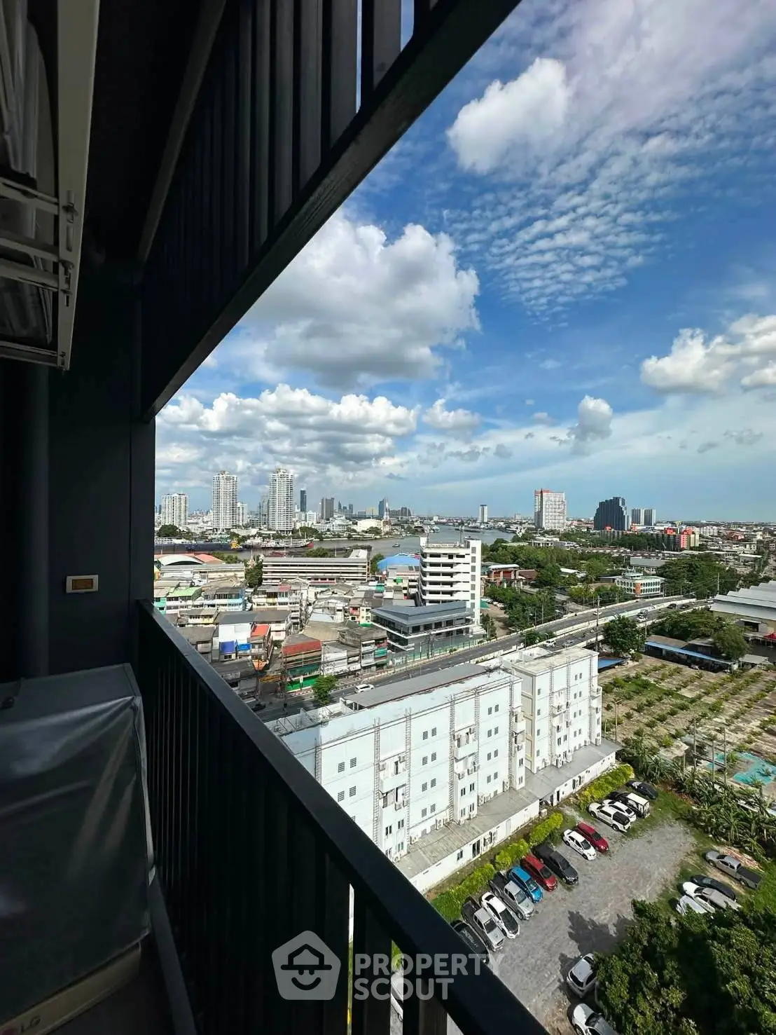 Stunning cityscape view from a high-rise balcony overlooking urban skyline and parking area.