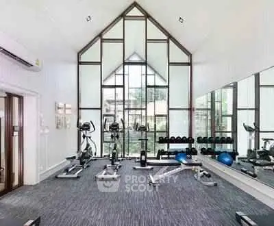 Spacious modern gym with large windows and fitness equipment in luxury residential building.