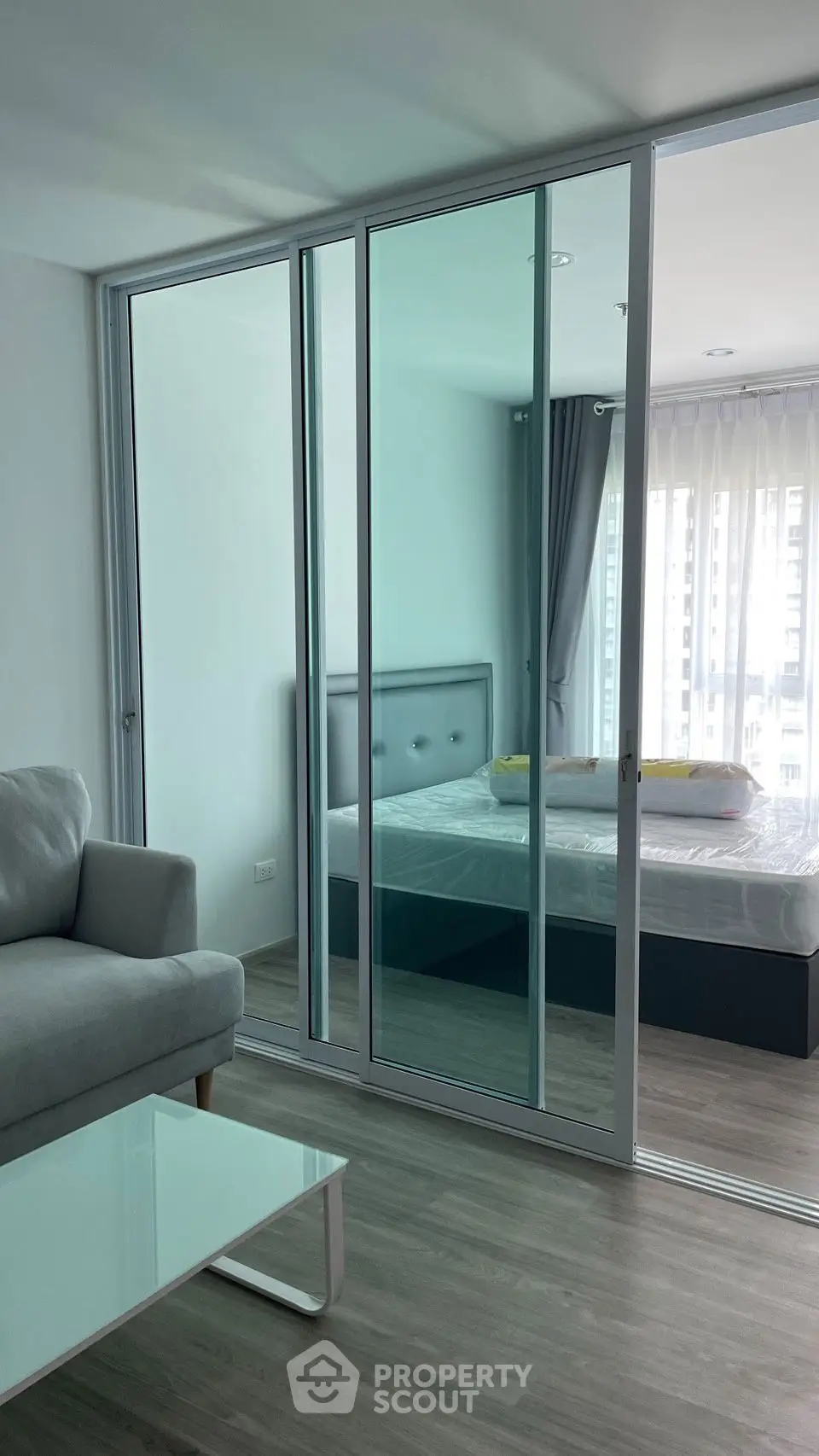 Modern apartment with glass sliding doors separating living room and bedroom, featuring sleek furniture.