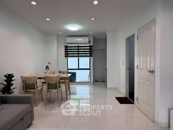 Modern living room with dining area and air conditioning, featuring sleek white tiles and contemporary furniture.