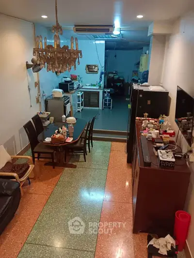 Spacious living room with dining area and open kitchen layout, featuring a chandelier and modern appliances.