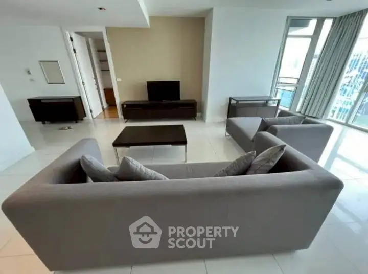 Spacious modern living room with sleek furniture and large windows offering city views.