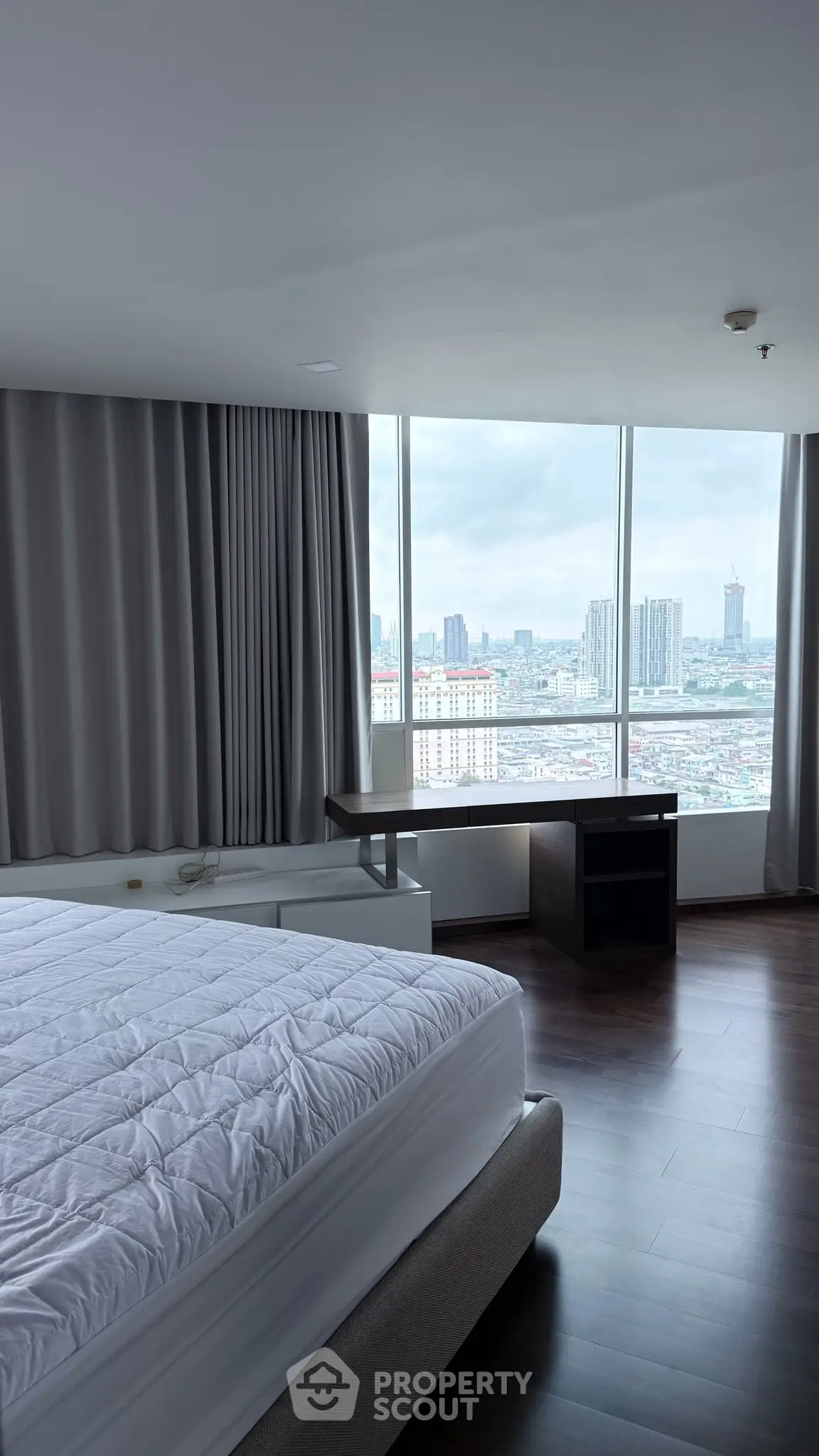 Spacious bedroom with panoramic city view and modern furnishings.