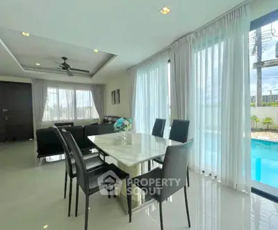 Luxurious open-plan living and dining area with pool view, featuring elegant furnishings and abundant natural light.
