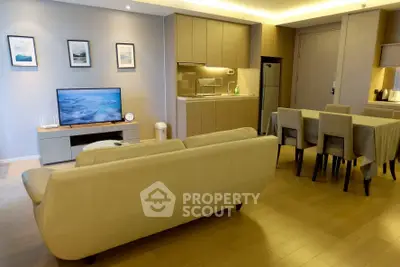 Modern open-plan living room with sleek kitchen and dining area, featuring stylish furniture and ambient lighting.