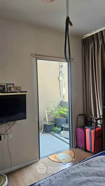 Cozy bedroom with TV and balcony access, featuring potted plants and natural light.
