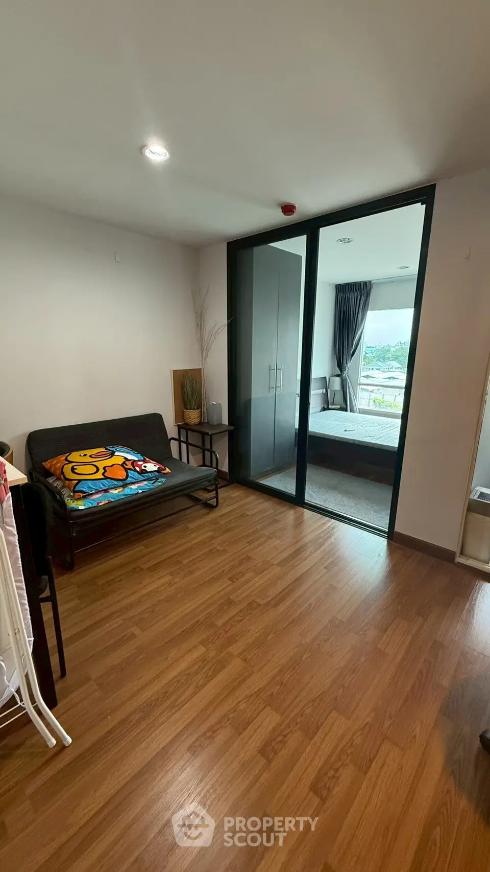 Modern apartment with wooden flooring and glass sliding doors leading to a cozy bedroom.