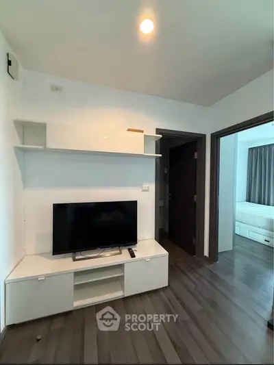 Modern living room with sleek TV unit and wooden flooring, adjacent to a cozy bedroom.
