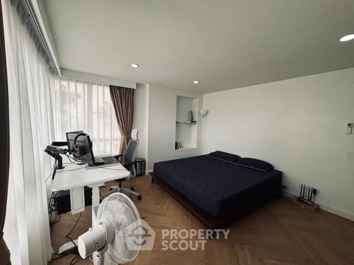 Modern bedroom with workspace and large window, featuring sleek furniture and natural light.