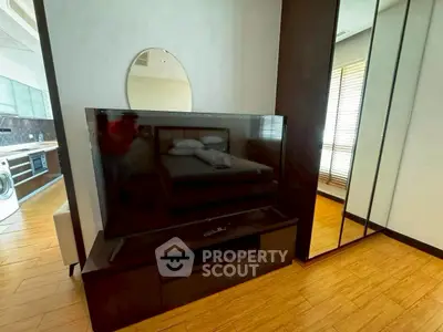 Modern apartment interior with TV, mirrored wardrobe, and wooden flooring.