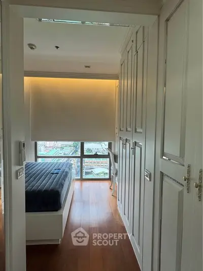 Cozy bedroom with city view, featuring elegant built-in wardrobes and warm wooden flooring.