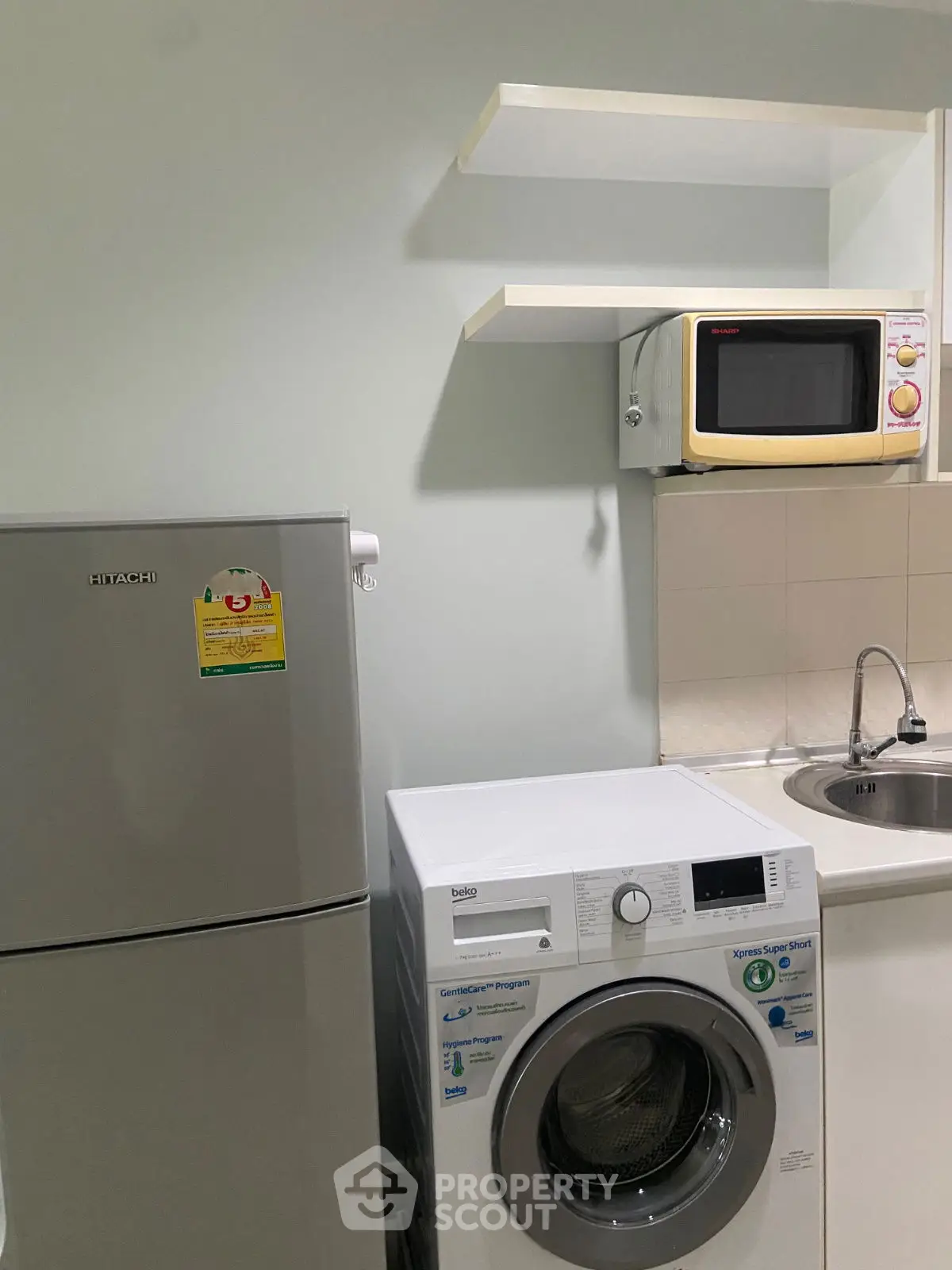 Compact kitchen with fridge, washing machine, and microwave setup.