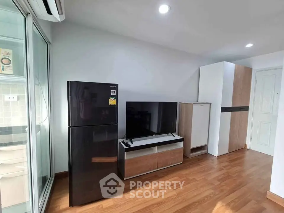 Modern living room with sleek black fridge and flat-screen TV on wooden floor.