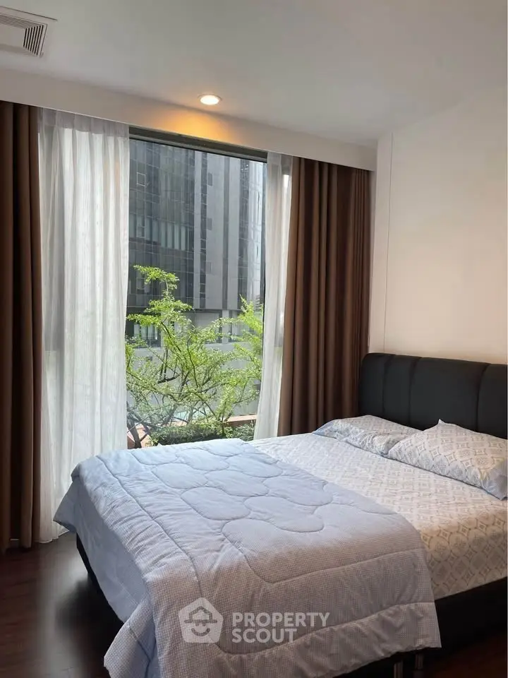 Modern bedroom with large window and city view, featuring cozy bedding and elegant curtains.