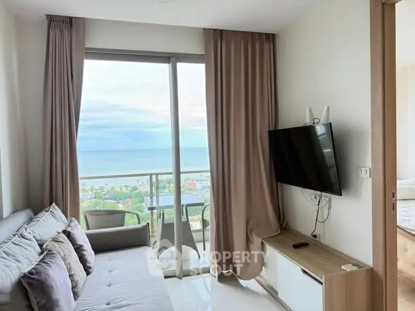 Modern living room with ocean view and balcony access, featuring sleek furniture and a mounted TV.