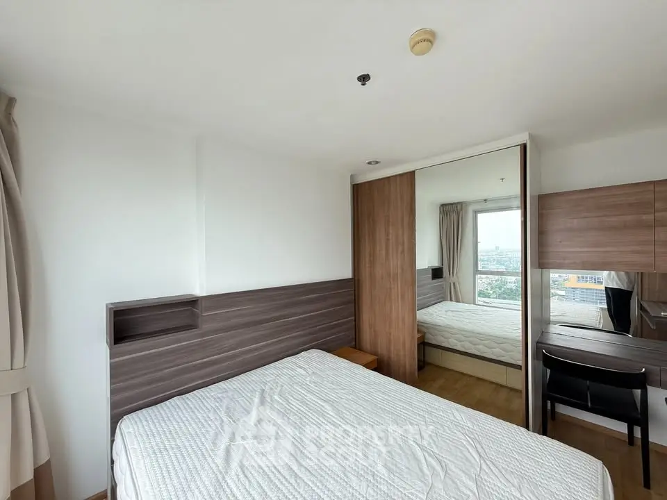 Modern bedroom with large mirror and city view, featuring sleek wooden accents and ample natural light.