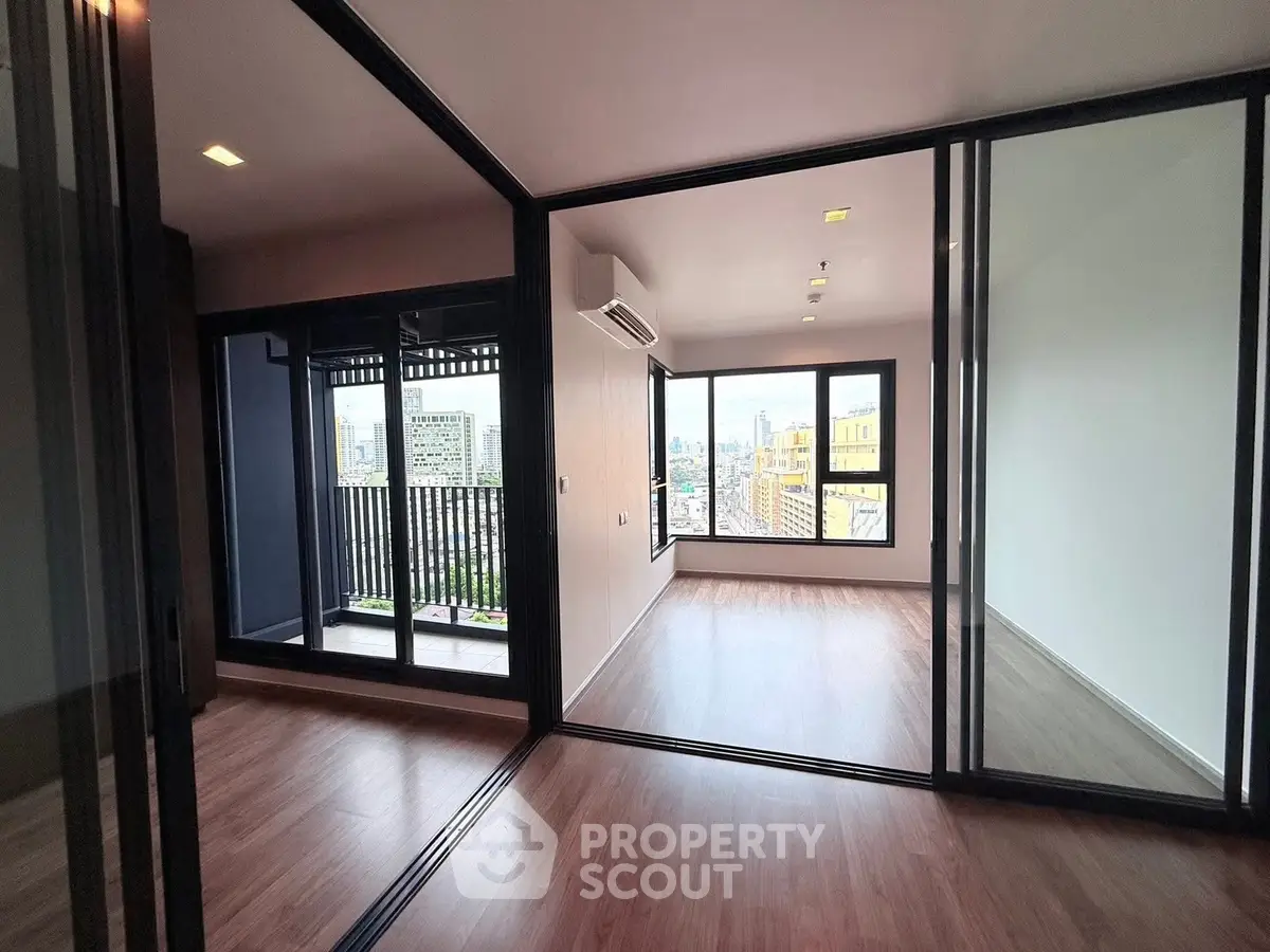 Spacious modern apartment with city view and large balcony, featuring sleek glass doors and wood flooring.
