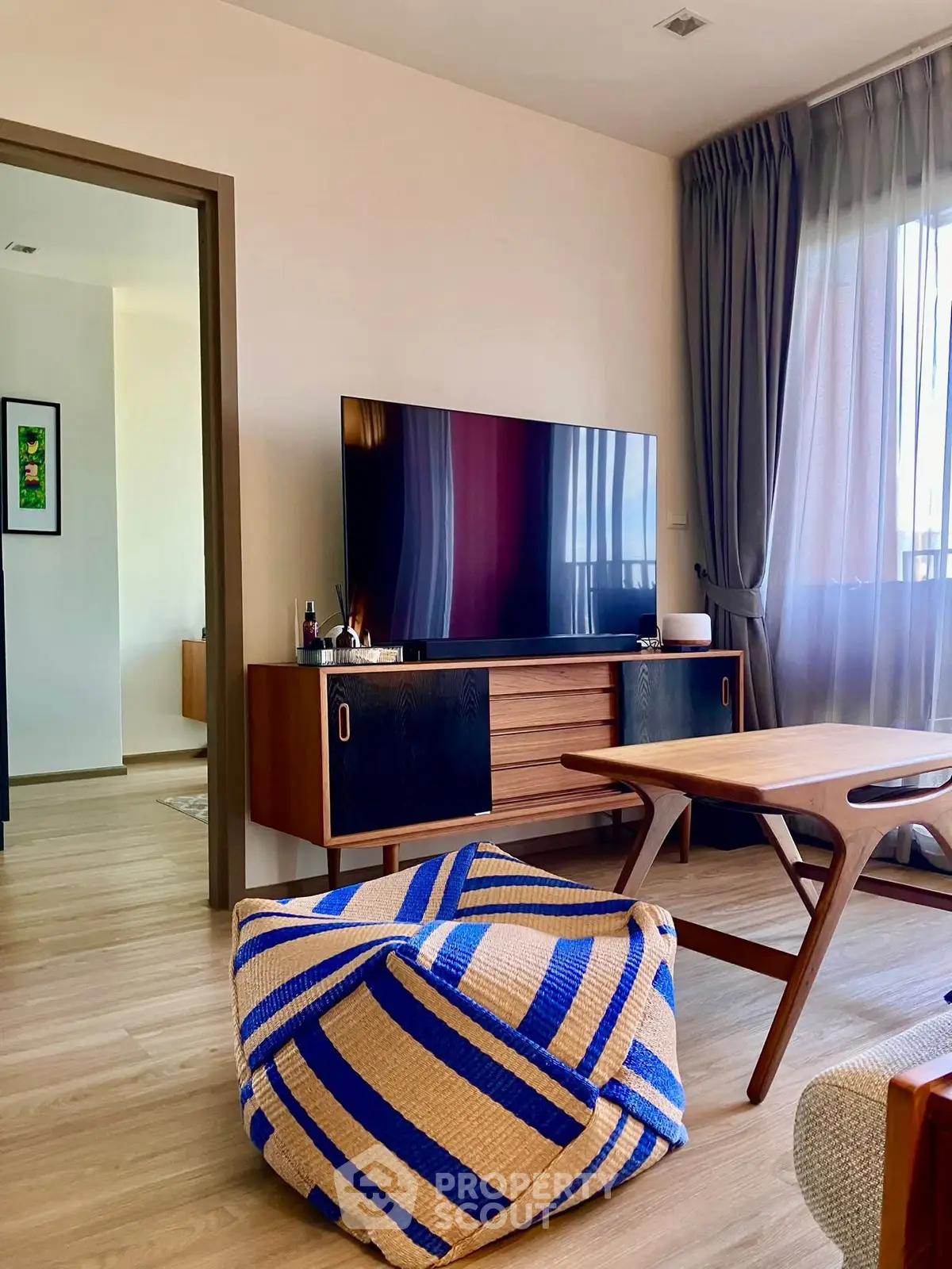 Modern living room with stylish furniture and large TV, featuring natural light and elegant decor.