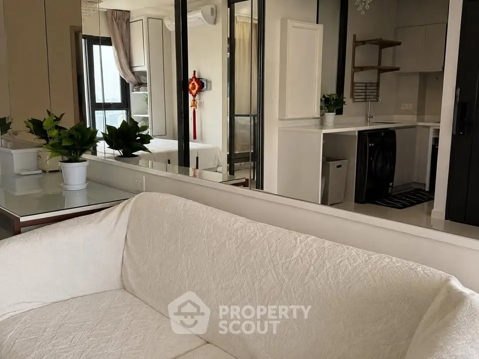 Modern living room with white sofa, mirrored walls, and compact kitchen area.