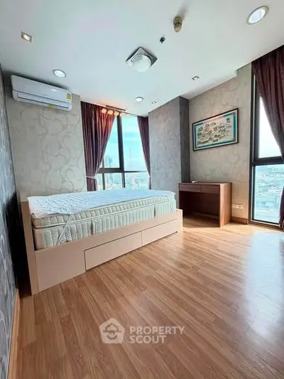 Spacious bedroom with large windows and wooden flooring in modern apartment.