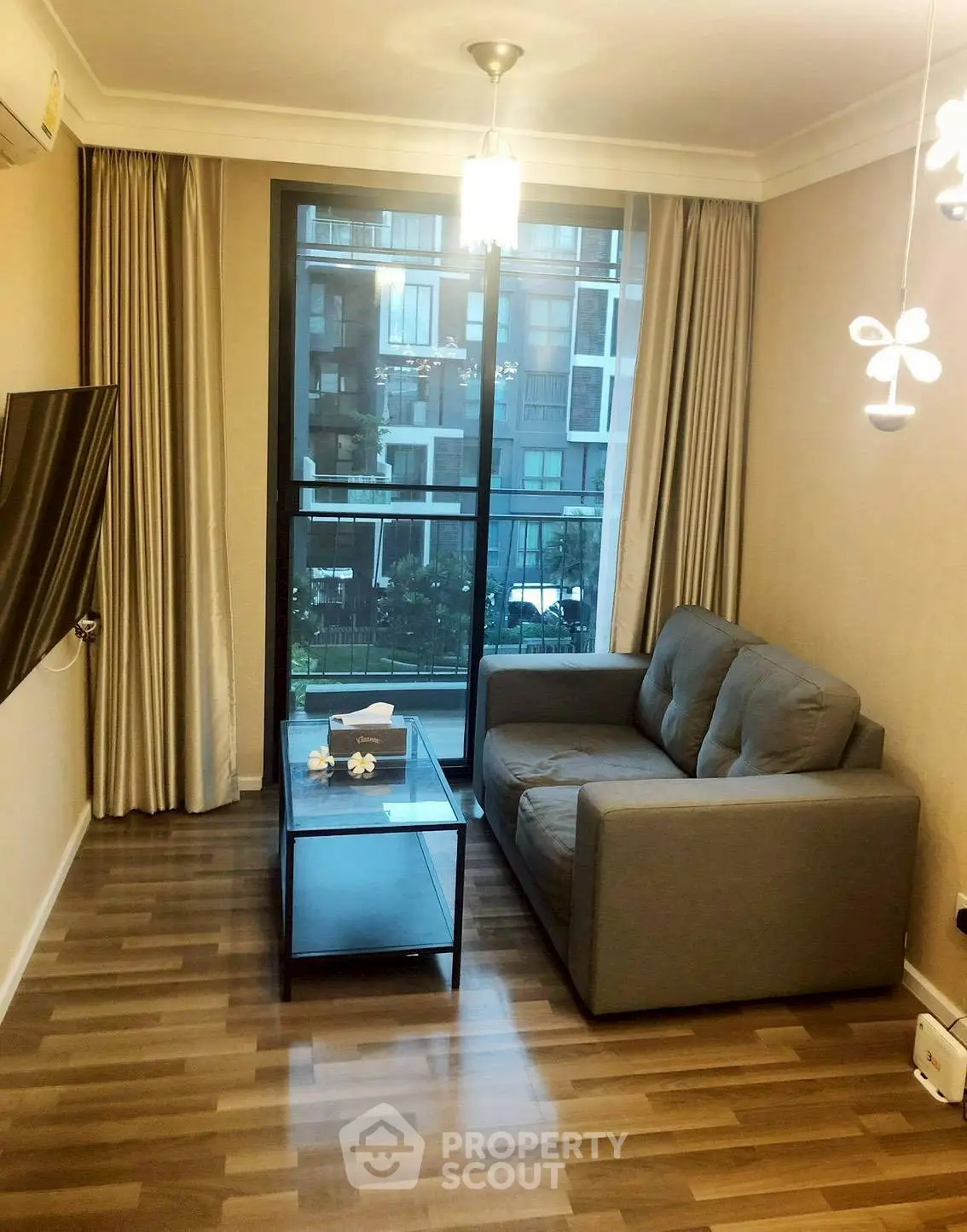 Cozy living room with modern sofa and glass coffee table, featuring a large window with city view.