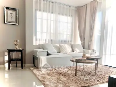 Elegant living room with plush rug and modern decor, featuring large windows and soft lighting.