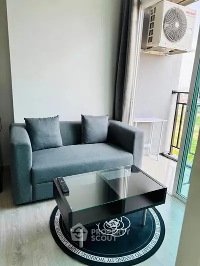 Modern living room with cozy sofa and glass coffee table near balcony with air conditioning unit.