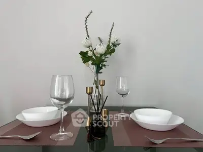 Elegant dining setup with glass table, white dishes, and floral centerpiece in modern home.