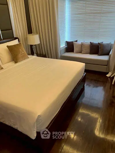 Elegant bedroom with polished wooden floors and cozy seating area by the window.