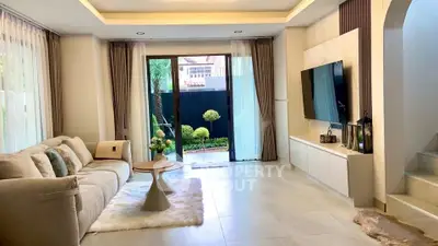 Elegant living room with modern decor and garden view, featuring cozy seating and stylish TV setup.