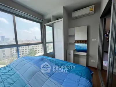 Modern bedroom with large windows and city view, featuring a blue bedspread and built-in wardrobe.