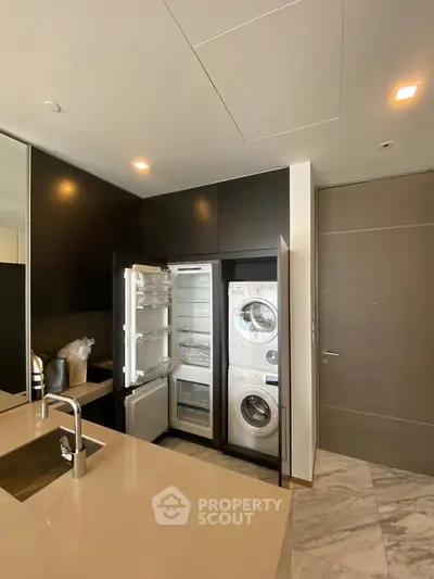 Modern kitchen with integrated appliances including fridge and washer-dryer, sleek cabinetry, and marble flooring.