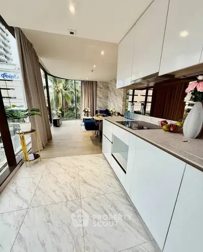 Modern open-layout kitchen with sleek cabinetry and spacious living area, featuring large windows and elegant decor.