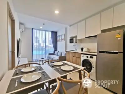 Modern kitchen with open layout flows seamlessly into cozy living space, featuring stainless steel appliances, sleek cabinetry, and a charming dining set perfect for urban living.