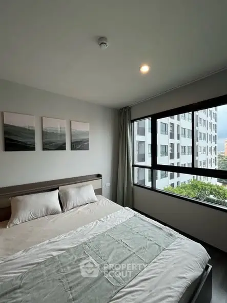 Modern bedroom with large window and city view in high-rise apartment.