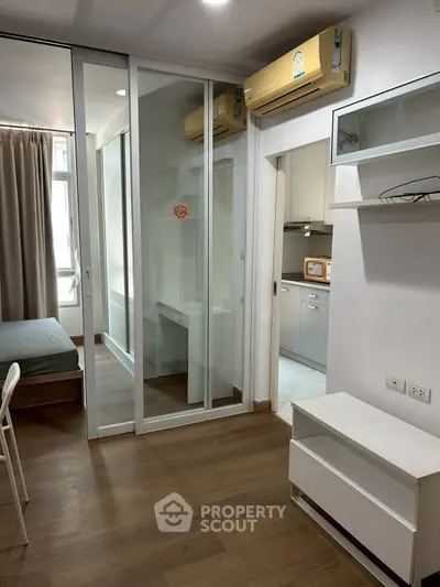 Modern apartment interior with sliding glass doors and air conditioning, featuring a cozy bedroom and kitchen area.
