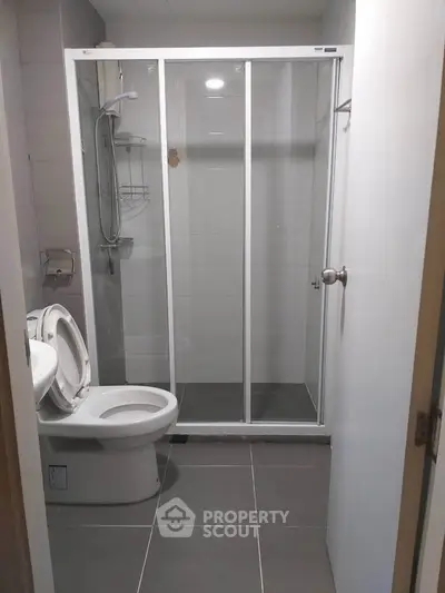 Modern bathroom with glass shower enclosure and sleek tile flooring.