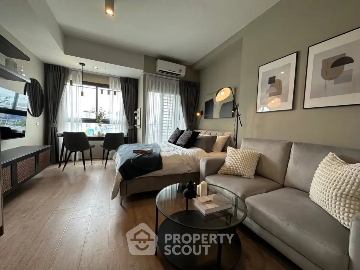 Modern studio apartment with stylish decor, featuring a cozy bed, elegant sofa, and dining area by large windows.